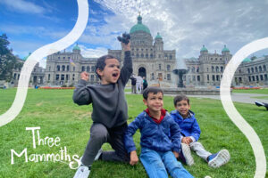 Three kids laughing and playing in front of the historic Parliament Buildings in Victoria, BC, with the iconic architecture and lush green lawn creating a picturesque backdrop